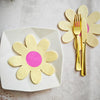 A white plate holds a yellow daisy flower napkin, next to a pair of gold disposable silverware.