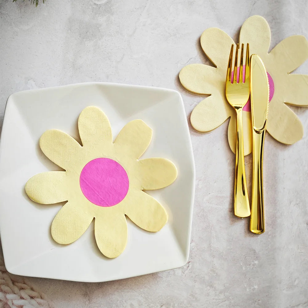 A white plate holds a yellow daisy flower napkin, next to a pair of gold disposable silverware.