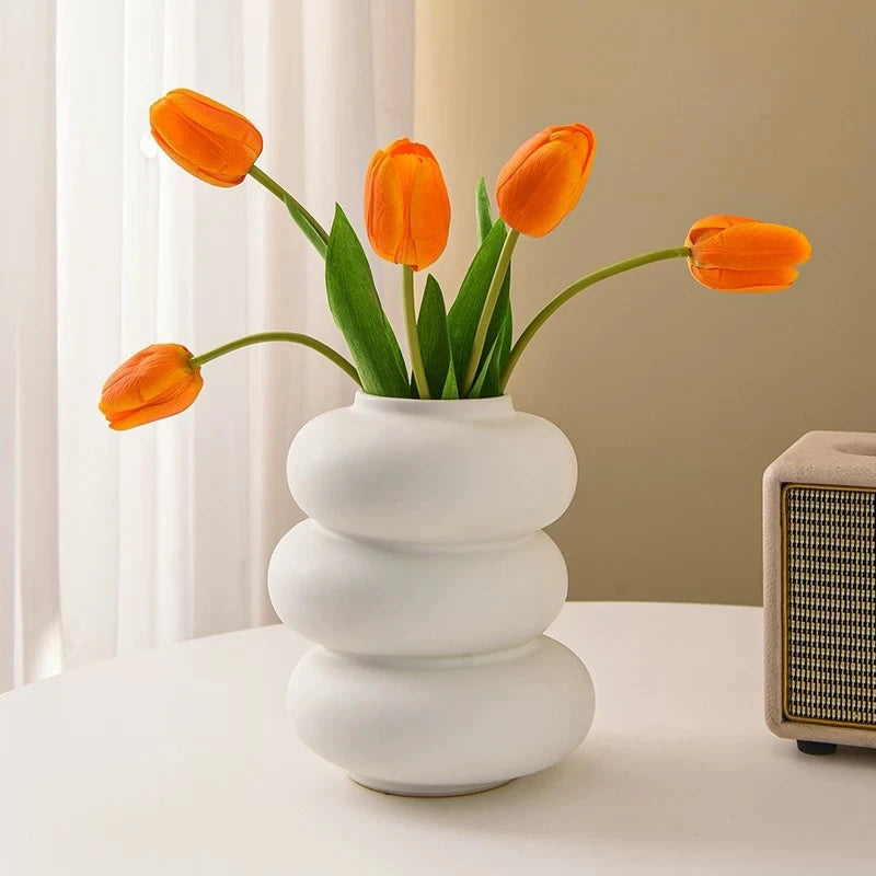 A vase of bright orange tulips in a modern white ceramic style on a light surface.