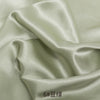 Close-up of smooth, lustrous satin fabric in a pale green color, showing draped folds.
