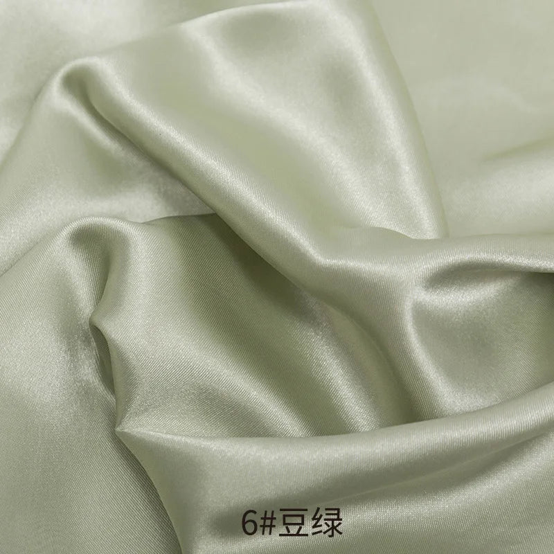 Close-up of smooth, lustrous satin fabric in a pale green color, showing draped folds.