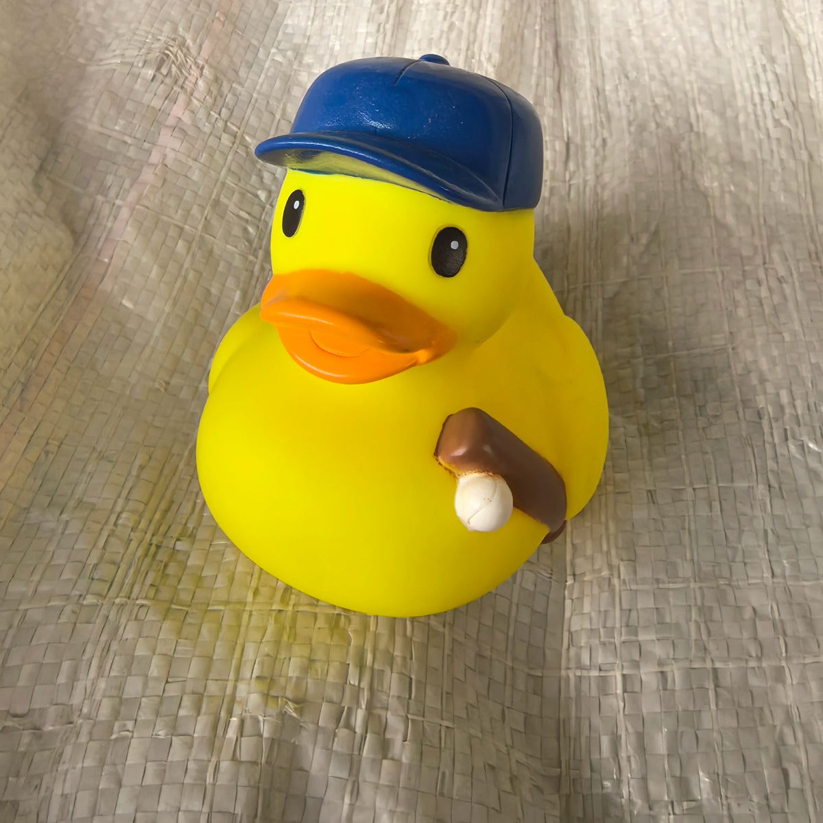 A yellow rubber duck toy wearing a blue cap is shown against a light, textured background.