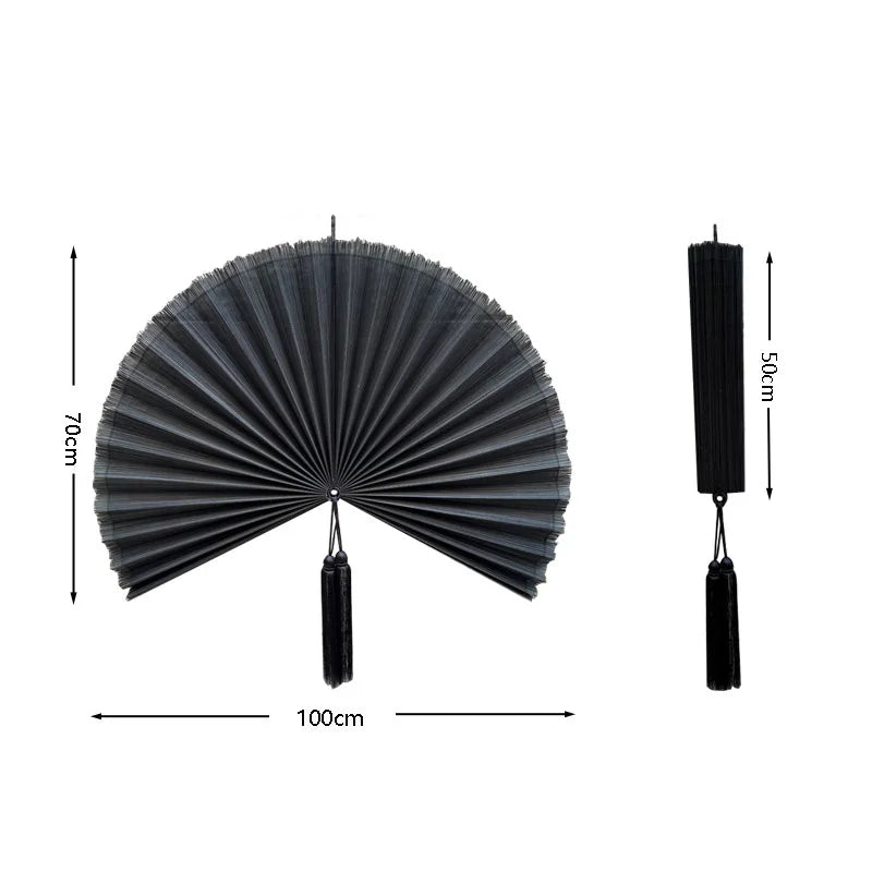 A black handwoven bamboo wall fan decor with a tassel, shown flat and with a hanging cord.