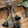 A set of decorative witch bells and a circular metal hoop with charms resting on a wooden surface.