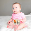 A baby sitting on a white surface looking to the side next to a wooden milestone card showing 8 months.