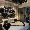 A bedroom decorated with black balloons spelling out Happy Birthday and love, featuring a bed with white linens.