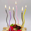 A display of curved metallic birthday cake candles in various shades of pink and yellow on a cake.