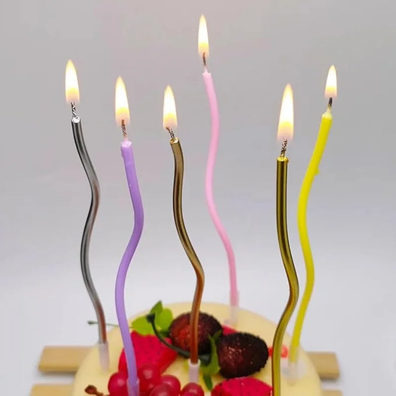 A display of curved metallic birthday cake candles in various shades of pink and yellow on a cake.