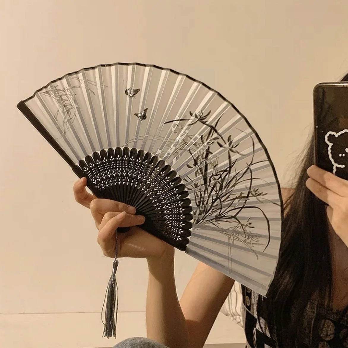 A hand holding an antique style bamboo folding fan with intricate black and white line art designs.
