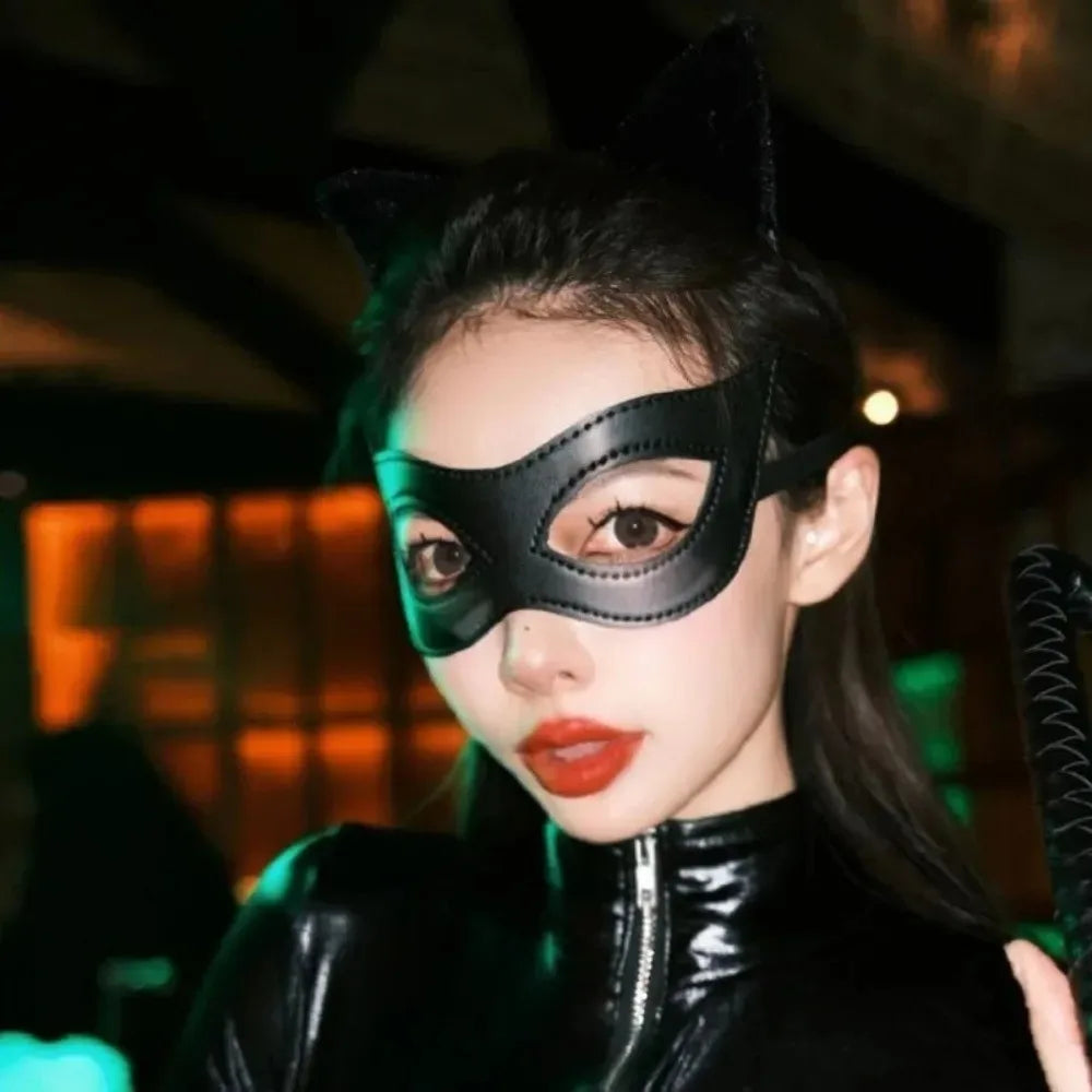 A woman wearing a black PU leather cat eye masquerade mask and a black leather outfit.