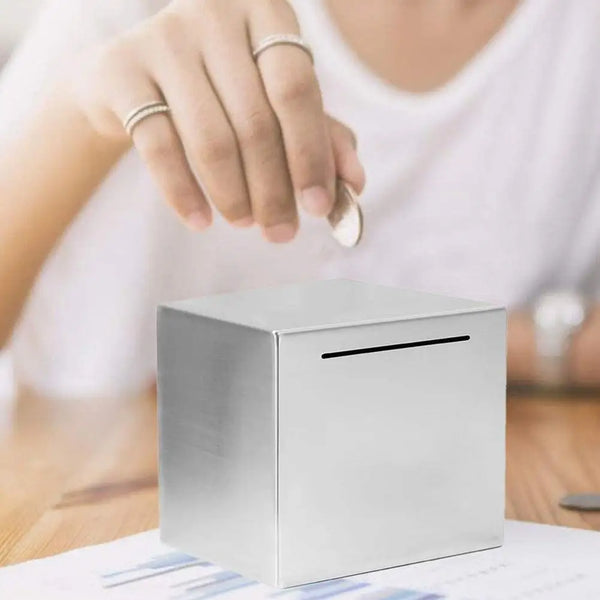 Une main pose une tirelire en acier inoxydable argenté sur une surface en bois.