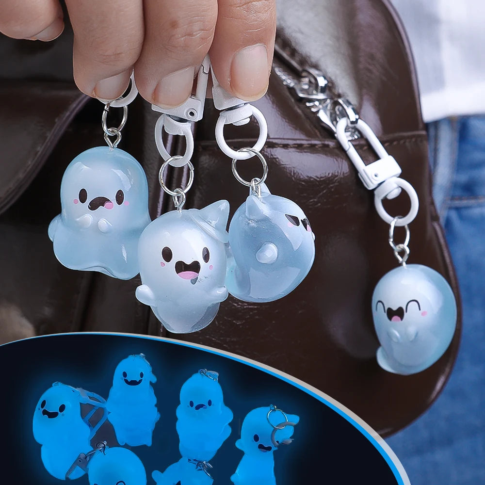 A hand holds a clear ghost-shaped glow-in-the-dark keychain featuring cute, smiling ghosts against a brown leather background
