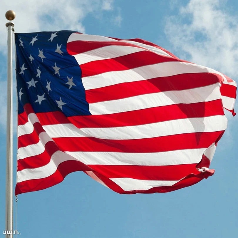 A large embroidered American flag waving outdoors against a blue sky.