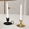 A tall white pillar candle in a black metal holder with a handle, set on a white table.