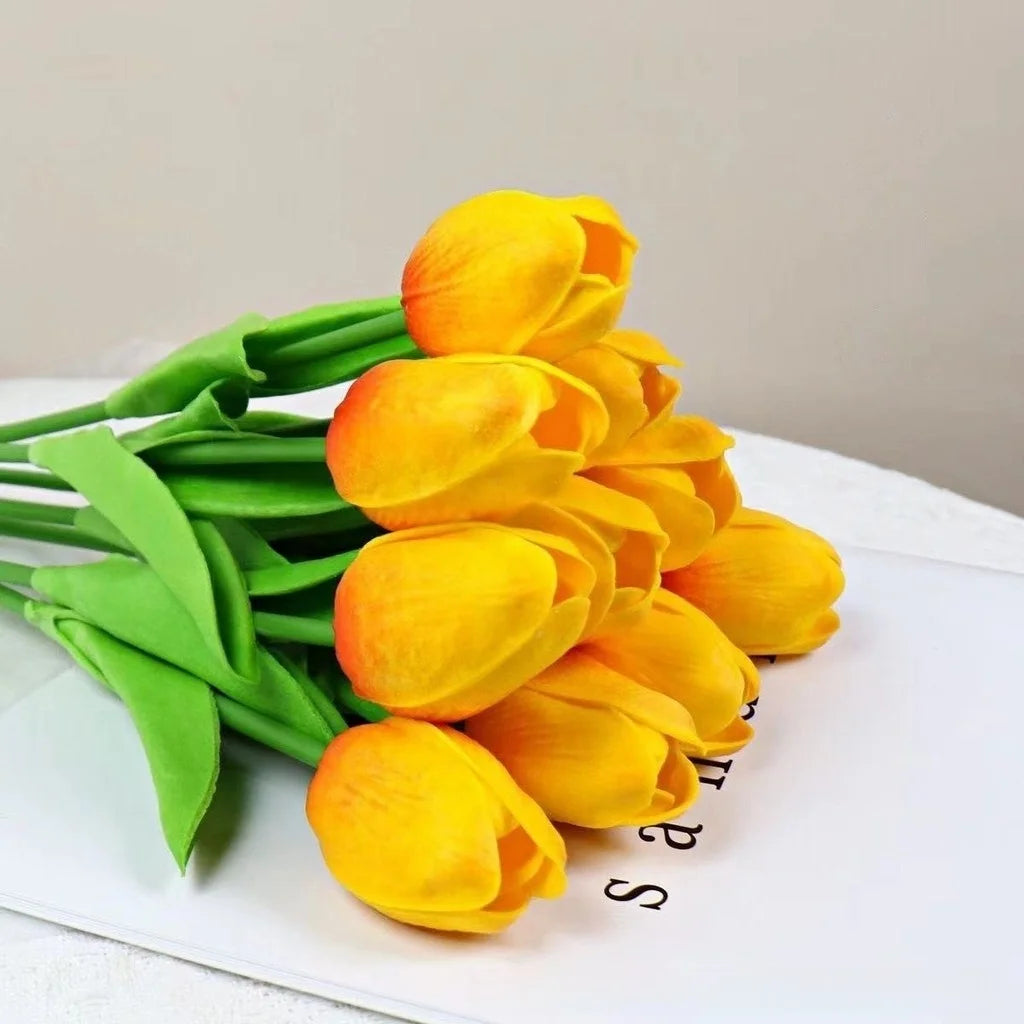 Un ramo de tulipanes artificiales amarillos brillantes con tallos verdes sobre una superficie blanca.