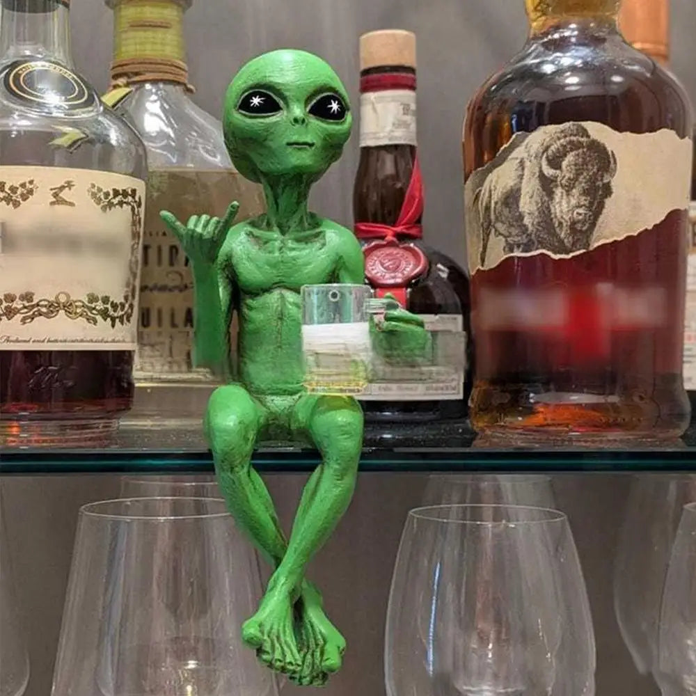 A green resin alien statue with a beer mug, displayed on a shelf among glass bottles.