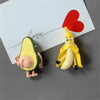 A set of cute 3D fruit fridge magnets featuring a banana and an avocado, with a red heart in the background.