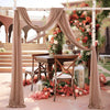 Two beige chiffon fabric panels draped on a wedding arch decorated with pink and orange floral arrangements.