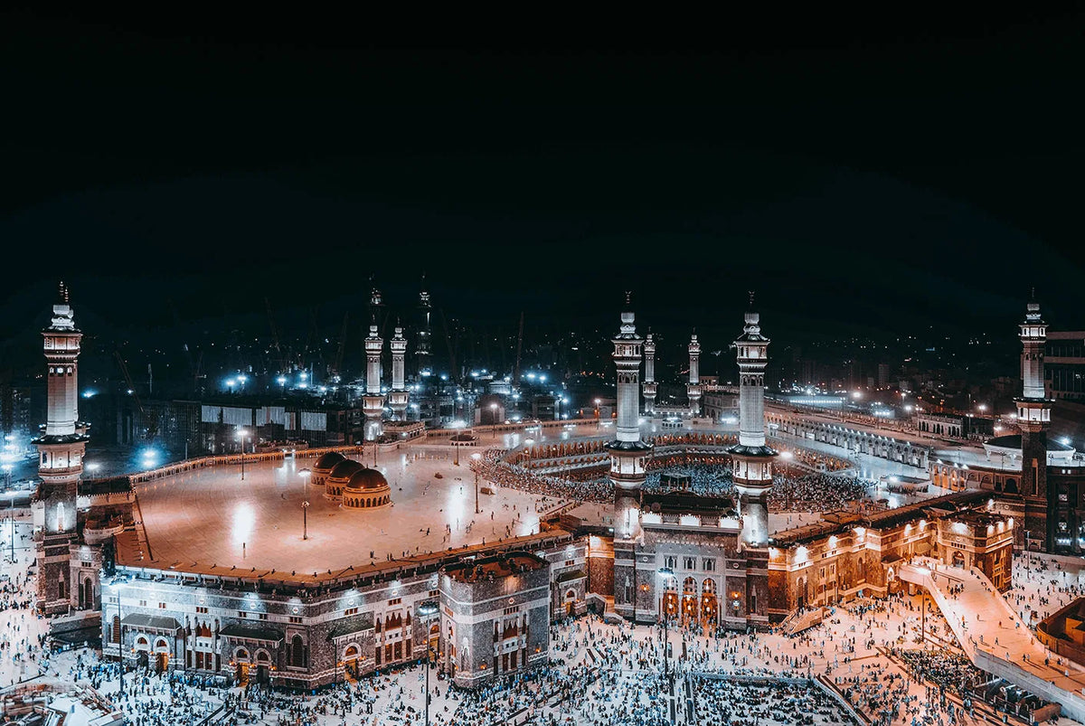 A panoramic night view of the Masjid an Nabawi in Mecca, showing architecture and crowds.