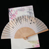 A vintage silk folding fan with delicate pink and gray oriental patterns is displayed on white paper.