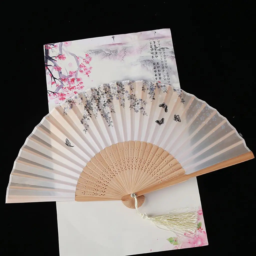 A vintage silk folding fan with delicate pink and gray oriental patterns is displayed on white paper.