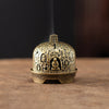 A vintage brass incense burner holder with a dome shape and small relief carvings sits on a wooden surface.