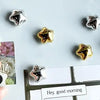A collection of gold star fridge magnets and a greeting card are displayed on a white surface.