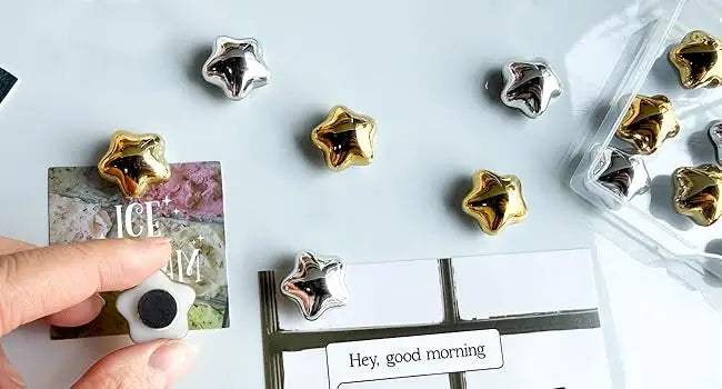 A collection of gold star fridge magnets and a greeting card are displayed on a white surface.