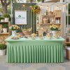 A long table covered with a light green pleated tablecloth set for an outdoor market or farm-to-table display.