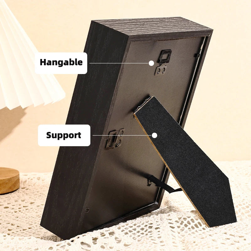 A black 3D shadow box frame is shown with hanging and support features, resting on a white lace surface.