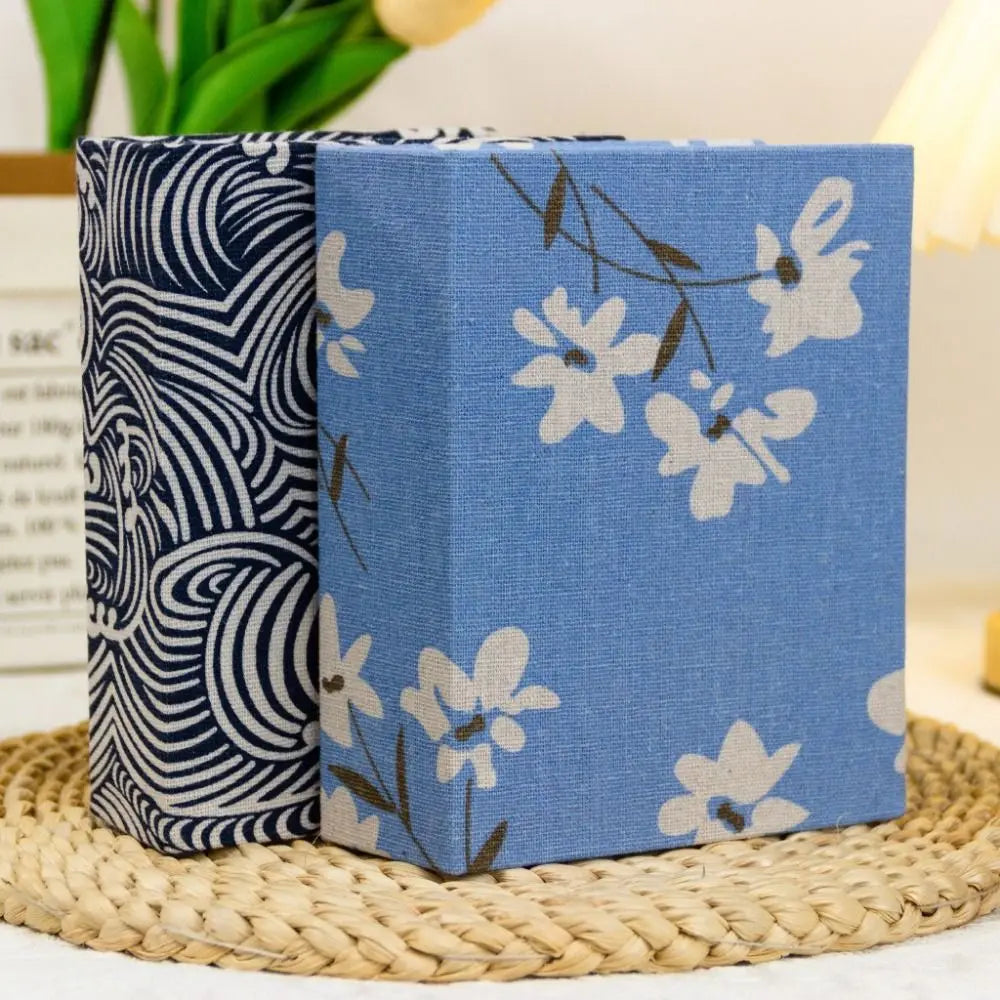 Ein Paar Leinen-Albumhüllen mit blau-weißen Blumenmustern auf einer gewebten Matte.