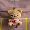 A Rilakkuma plush bear keychain is hanging from a tag on a pink fabric bag.