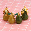 Three pear-shaped fruit keychains with gold findings and glittery green and gold finishes on a pink grid background