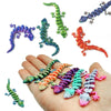 A hand holds several colorful 3D printed articulated gecko desk toys in various poses and colors.