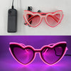 Pink heart-shaped LED wire party glasses glowing bright pink in a purple light.