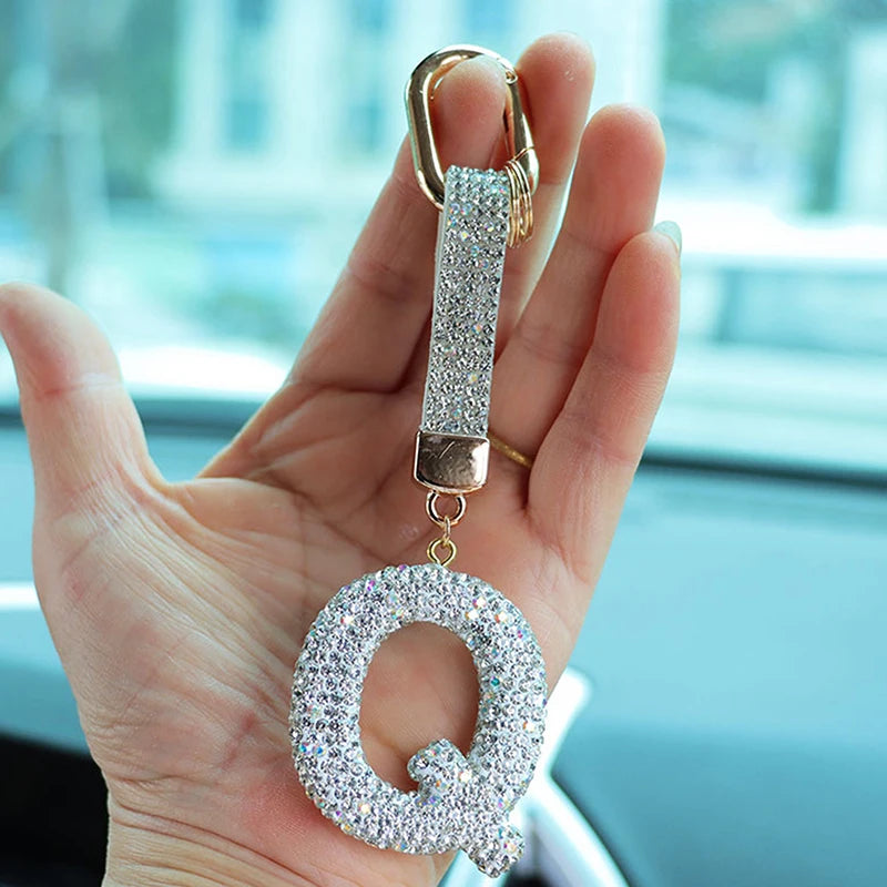 A hand holds a crystal letter keychain charm shaped like the letter Q