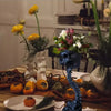 Dunkelblaue gotische Schädel-Topf-Dekoration mit Blumen und herbstlichen Früchten auf einem Holztable