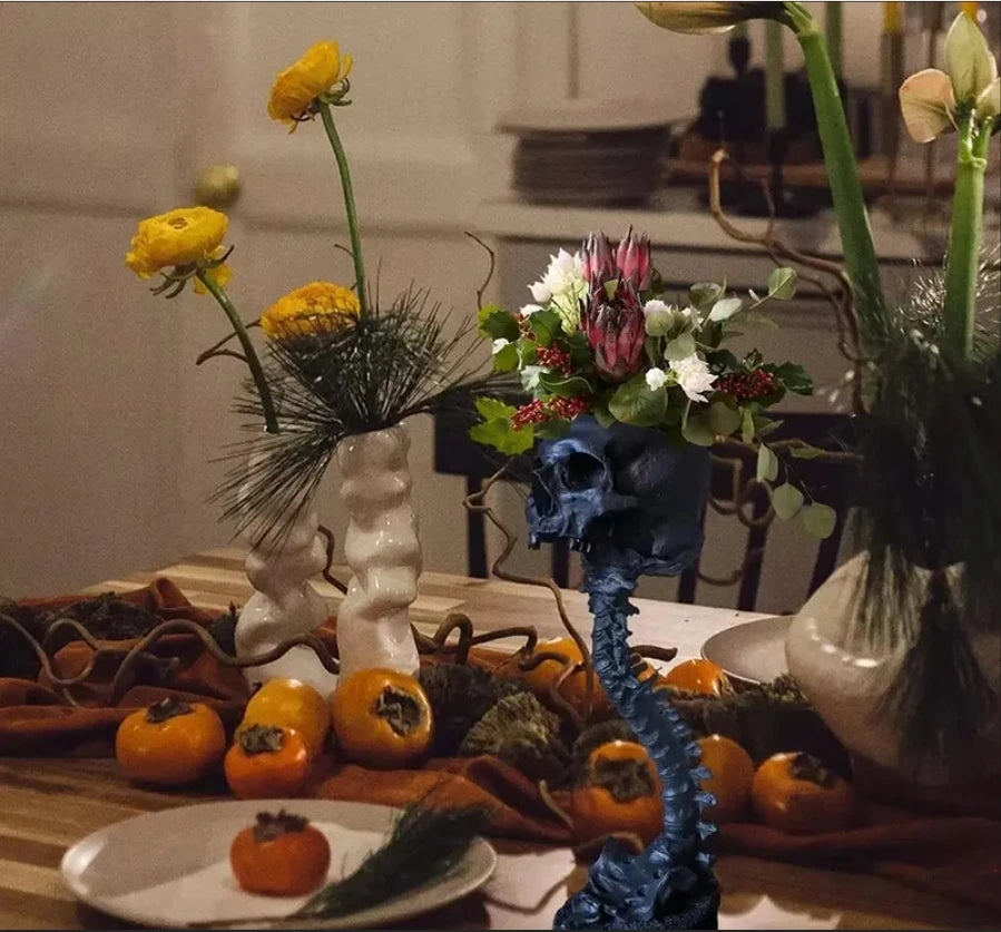Dunkelblaue gotische Schädel-Topf-Dekoration mit Blumen und herbstlichen Früchten auf einem Holztable