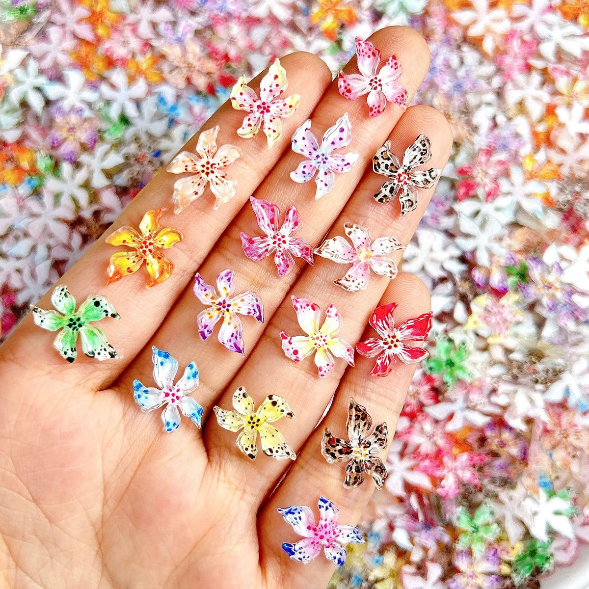 Una mano muestra 50 adornos de uñas de tortuga mini coloridos con diseños florales sobre un fondo texturizado.