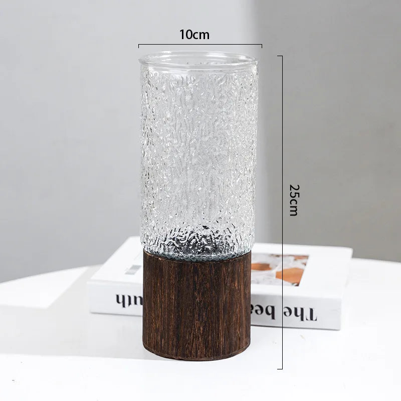 A clear glass vase with a textured surface and a dark wooden base, shown standing upright.
