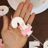 Una mano sostiene una vela mágica rosa y blanca decorada con purpurina y una pequeña figura.