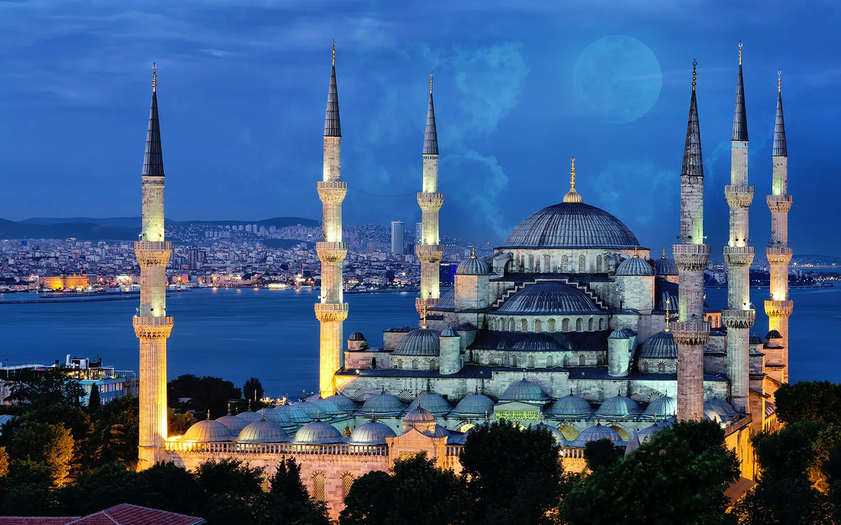 A nighttime view of a mosque with minarets and a large dome silhouetted against a twilight sky.