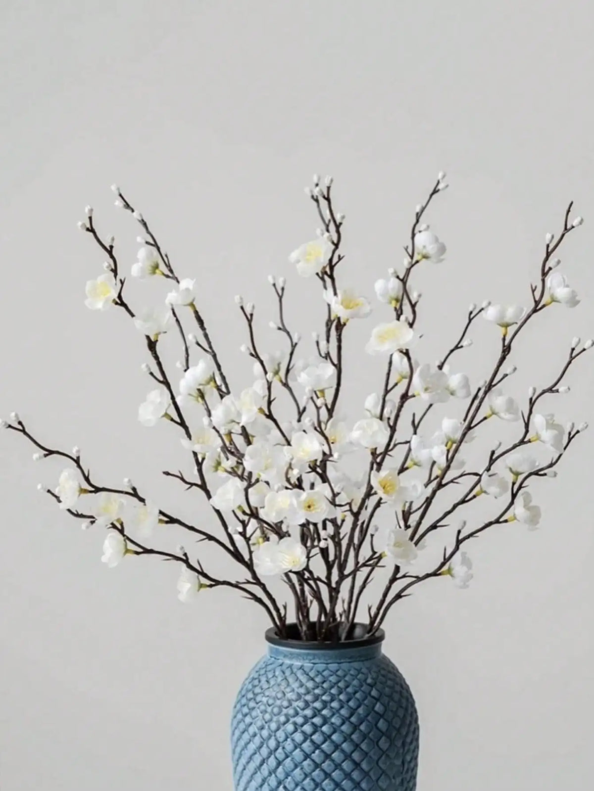 Ramitas de flor de ciruela blanca artificial en un jarrón de cerámica azul para decoración del hogar