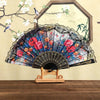 A Spanish style folding lace trim handheld fan with a dark fabric and floral patterns displayed against a light background.