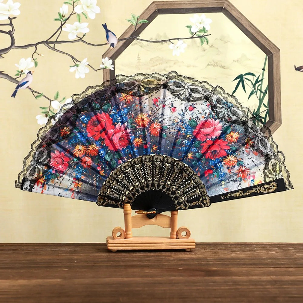 A Spanish style folding lace trim handheld fan with a dark fabric and floral patterns displayed against a light background.