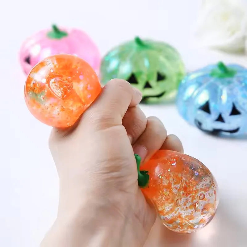 A hand is squeezing an orange Halloween pumpkin stress ball, surrounded by other decorative pumpkins.