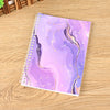 A purple and gold marbled reusable sticker collecting album with a spiral binding lying on a wooden surface.