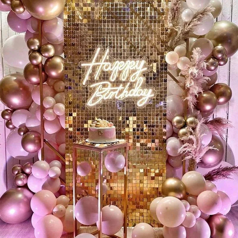 A shimmering gold glitter square wall backdrop decorated with pink and gold balloons and a glowing birthday sign.