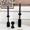 A set of two black, twisted candle holders with a lit candle on a white surface.
