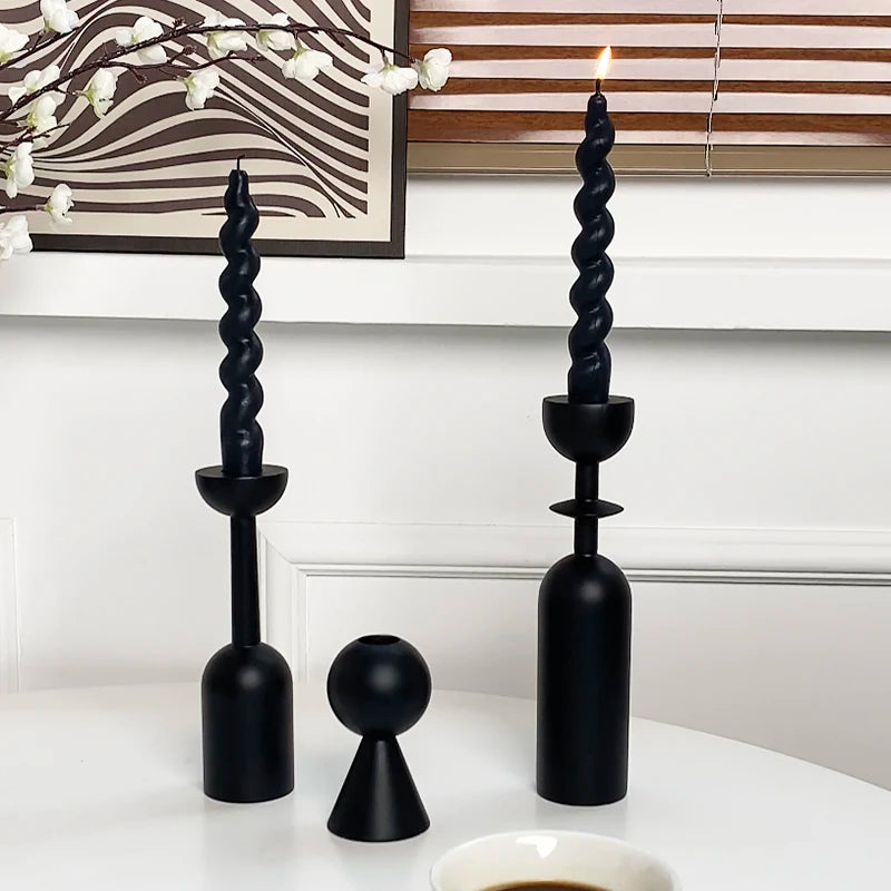 A set of two black, twisted candle holders with a lit candle on a white surface.